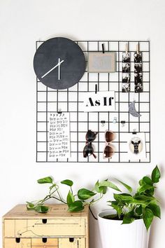 a clock mounted to the side of a white wall next to a potted plant