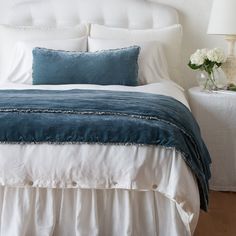 a white bed topped with pillows and blankets next to a night stand filled with flowers