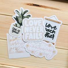 some stickers are sitting on top of a wooden table and one is saying love never fail