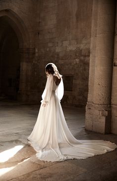 a woman in a white wedding dress is standing near an archway and wearing a veil