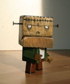 a wooden toy with eyes and hands holding a piece of wood in the shape of a robot