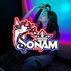 a woman sitting on the floor in front of a neon sign that says sonam