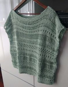 a green knitted sweater hanging on a wooden hanger in front of a white cabinet