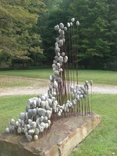 a sculpture made out of rocks and sticks in the grass with trees in the background