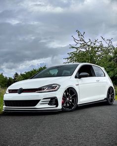 a white car parked on the side of a road next to some grass and trees