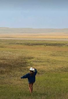 a woman in a blue dress and hat is flying a kite on the open field