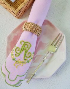 a pink napkin with a monogrammed initial sits on a plate next to a fork and knife