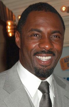 a close up of a person wearing a suit and tie smiling at the camera with lights in the background