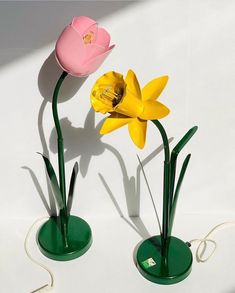 two yellow and pink tulips in green vases on a white table top