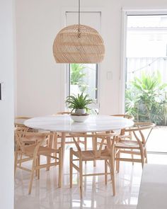 a dining room table with chairs and a potted plant in the center, next to a large window