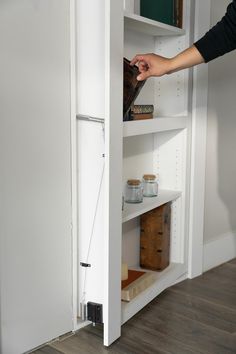 a person is opening the door to a white pantry with lots of items in it