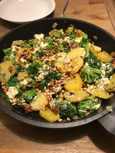 a pan filled with broccoli, potatoes and other food on top of a wooden table