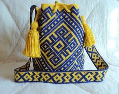 a blue and yellow bag with tassels on the handles sitting on a white surface