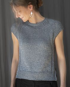 a woman standing in front of a gray background wearing a grey sweater and black pants