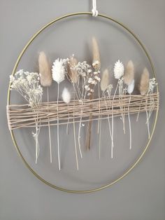 a circular metal frame with dried flowers on it, hanging from the wall in front of a gray wall