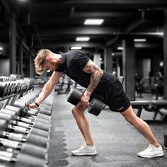 a man doing squats with dumbbells in a gym area, while looking down at the floor