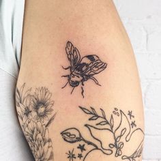 a woman's arm with a bee and flowers tattoo on the left side of her body