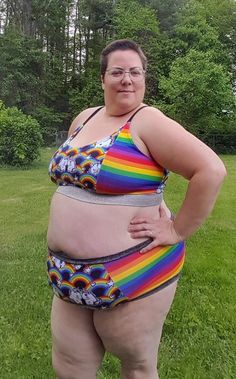 a woman in a rainbow colored swimsuit standing on grass with her hands on her hips