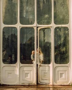 two children are standing in the open doors of a building that has glass panes