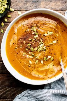 a white bowl filled with soup and topped with pumpkin seeds on top of a wooden table