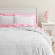 a bed with pink and white comforters in a bedroom next to a night stand