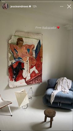 a painting hangs on the wall next to a chair and ottoman in a white room