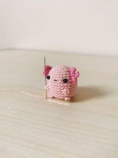 a small pink crocheted animal holding a needle in it's mouth on top of a wooden table