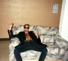 a man sitting on top of a couch with his hand in the air while wearing sunglasses