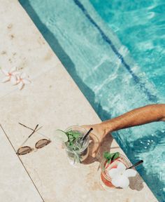 a man holding a drink next to a swimming pool with flowers in the glass and spoons