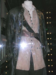 a man's coat and hat are on display in a glass case with lights behind it