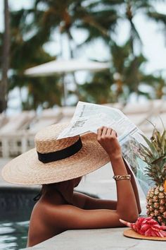 a woman sitting next to a pool reading a newspaper and holding a pineapple in her hand