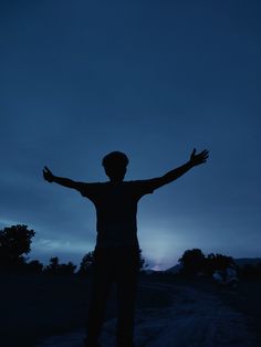 a person standing on a dirt road with their arms wide open in the night sky