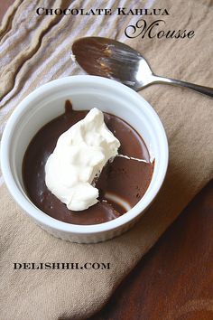 a bowl filled with chocolate pudding and whipped cream on top of a wooden table next to a spoon