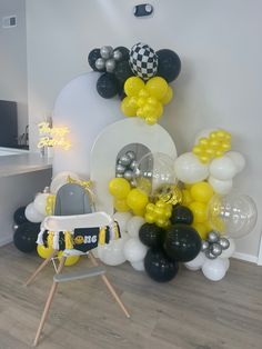 a room filled with balloons and black and white decorations on the wall, along with a baby's highchair