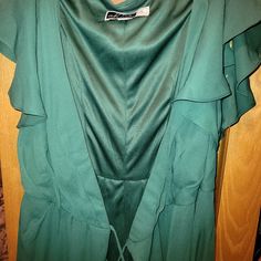 a green blouse with ruffles hanging on a wooden closet door in front of a wood paneled wall