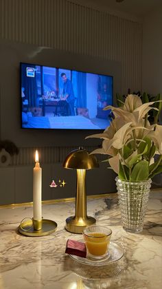 a table topped with a vase filled with flowers next to a candle and a flat screen tv