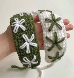 two crocheted wristbands with green and white flowers are held in the palm of someone's hand