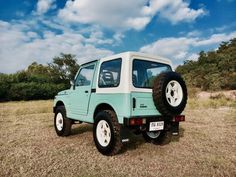 a light blue and white jeep parked on top of a grass covered field with trees in the background