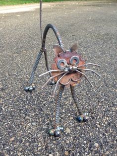 a metal cat sculpture sitting on top of a gravel road