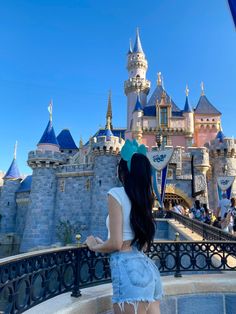 a woman standing in front of a castle with her back to the camera and looking at it