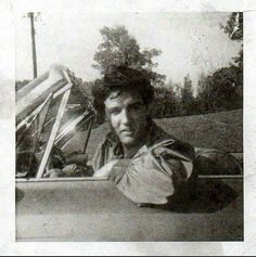 black and white photograph of a man leaning on the hood of a car