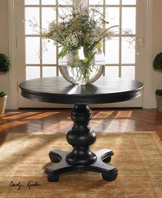 a vase with flowers on top of a table in front of an open window and rug