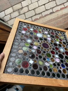 a person holding a wooden frame filled with lots of different colored glass bottles