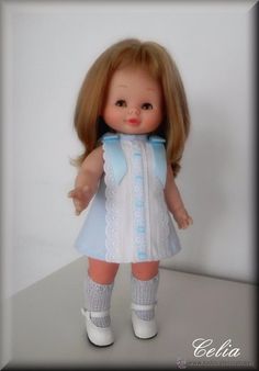 a doll with blonde hair wearing a white dress and blue collared necktie, holding her hands out to the side