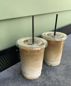 two iced coffees sitting on the ground next to each other with black straws