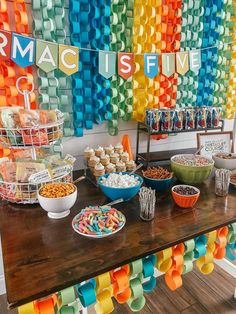 a table topped with lots of food next to colorful streamers hanging from the ceiling