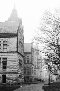 black and white photograph of an old brick building on a foggy day with trees in the foreground