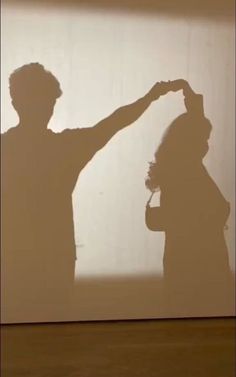 the shadow of two people standing in front of a wall with their hands on their hips