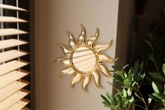 a sun shaped mirror mounted to the side of a wall next to a potted plant