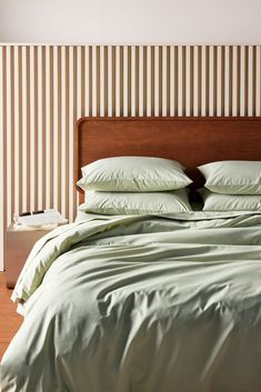 a bed with green sheets and pillows in a room that has striped wallpaper on the walls